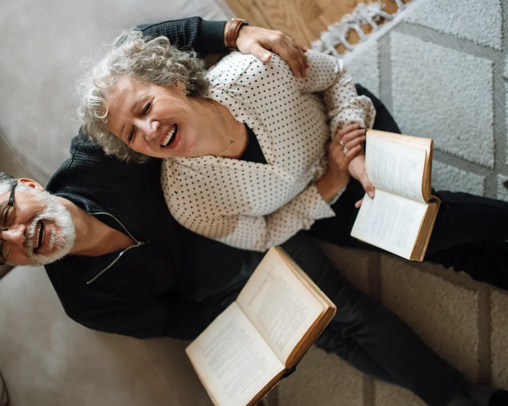 An older couple laughing together on the sofa at home